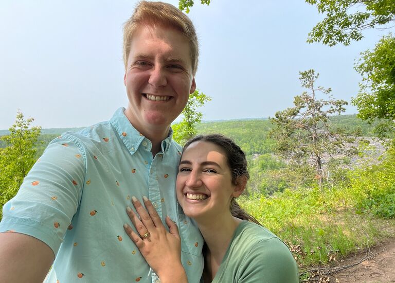 Andrew went on a Caribbean cruise with his family in early June, and decided this would be the perfect opportunity to find an engagement ring for Maddie. When he returned and went to see Maddie at her parents' house, he asked their permission to marry Maddie and showed them the ring. They were thrilled, and so the next day, Andrew took the ring with him when he and Maddie when hiking at Jay Cooke State Park. When they got to an overlook of the river, Andrew decided this was the perfect place and time to ask Maddie to marry him. He turned to Maddie and said, "Hey, I love you a lot, and I want to keep loving you for a long time." Maddie then kissed Andrew and he thought, 'This is great, but I was trying to do something there.' Then a family showed up at the overlook, and Andrew realized his window had closed. Maddie saw he was a little bummed they had ruined their moment, and she said, "This isn't even the main spot." Hope was reignited for Andrew! When they got to main overlook, Andrew turned to Maddie and said, "Hey, I love you a lot, and I want to keep loving you for a long time." Maddie jokingly responded by saying, "What, are you gonna propose?" "Actually, yeah," Andrew responded. He proceeded to pull out the ring and get down on one knee. "OH MY GOSH!" Maddie exclaimed. "Is this real?! Is this a joke?!" Andrew assured her it wasn't, and after kneeling for awhile, said, "I'm waiting on an answer." "You haven't asked a question," responded Maddie. Andrew realized in all the excitement, he had not, in fact, explicitly asked Maddie to marry him. He quickly fixed that problem, and Maddie enthusiastically said yes.