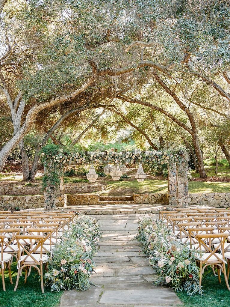 Rustic outdoor wedding ceremony with cross-back chairs and stone arch