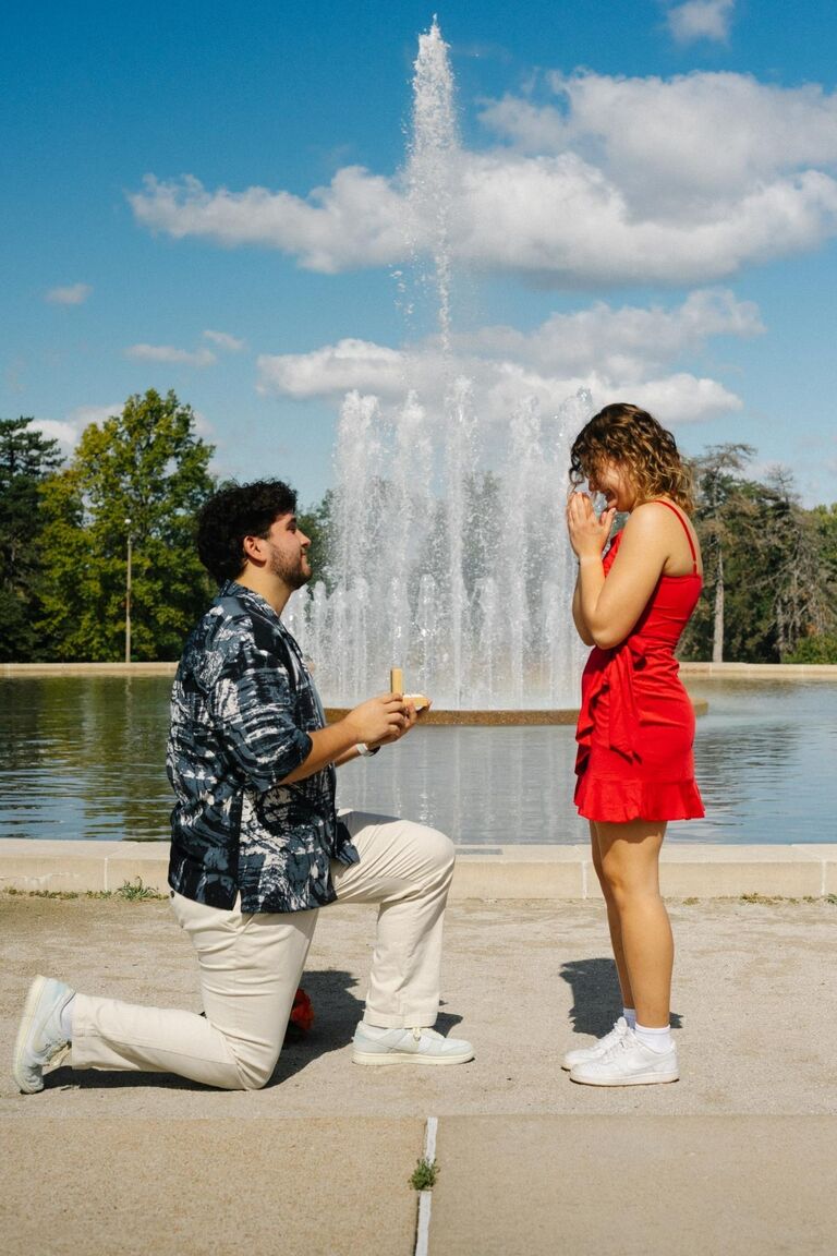 While Eliana thought Jacob was working in Minneapolis, he was actually driving down to St. Louis to propose. Eliana thought she was going on a picnic in Forest Park with her friends. When she got there, she was shocked to see Jacob standing in front of a fountain with a bouquet of flowers. She ran down a hill, gave him a hug, and said yes!