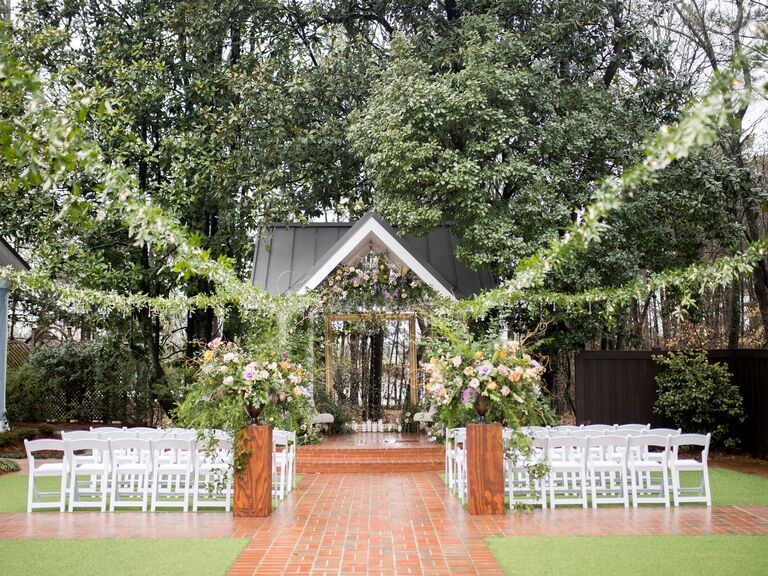 Charming outdoor ceremony space with hanging foliage and white lawn chairs
