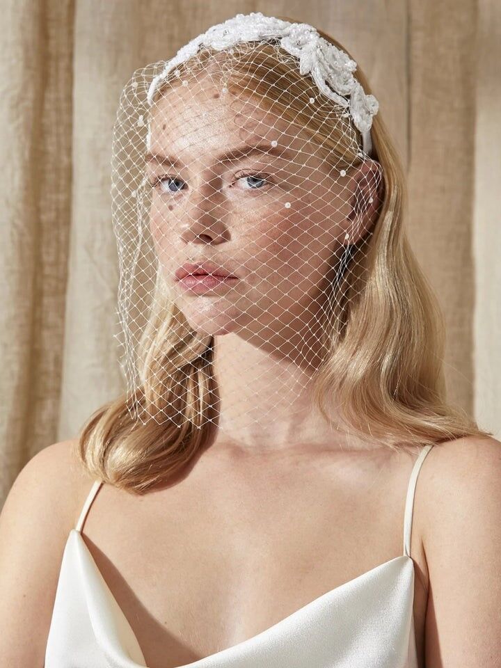 Model wears a birdcage veil attached to a floral detailed headband. 