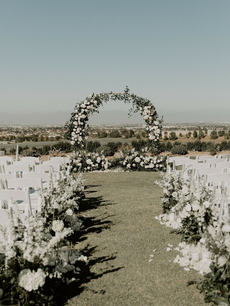 Outdoor ceremony with white chairs and flower-covered circle arch