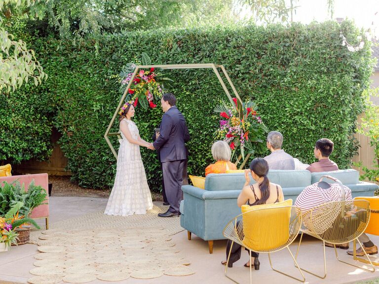 Couple exchanging vows in backyard in front of gold hexagon arch
