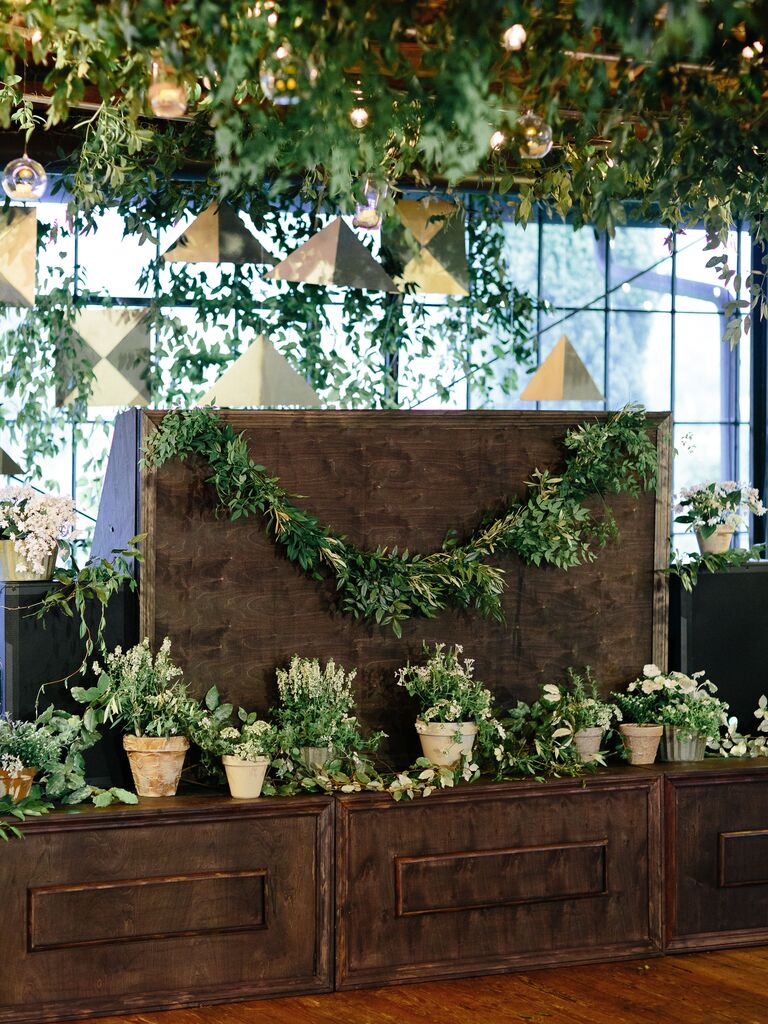 wedding DJ booth decorated with greenery garland and white potted plants in terracotta pots