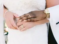 Close up of groom hugging bride form behind while wearing wedding rings