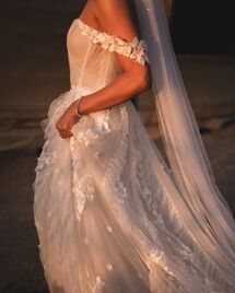 Side profile of a wedding dress with 3D floral lace and ruffled tulle sleeves, illuminated by warm sunset light.
