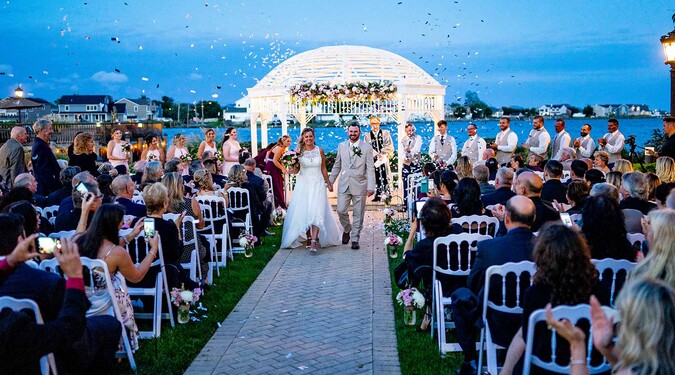 Bride and groom walking down aisle after outdoor waterfront ceremony with confetti at Riviera Waterfront Mansion