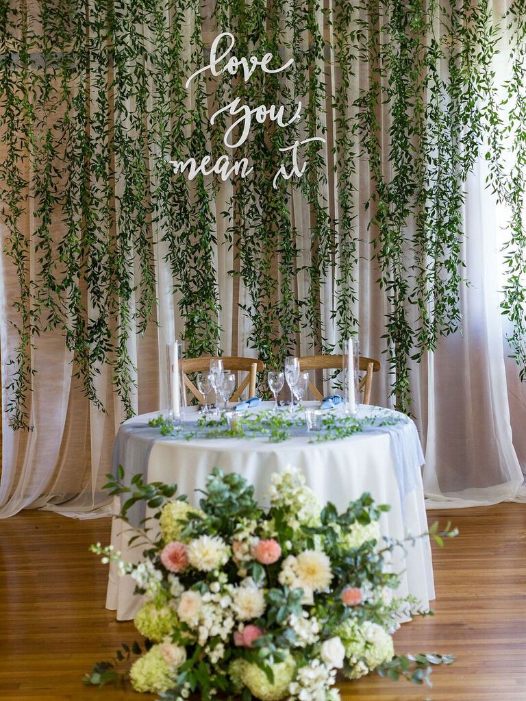 Sweetheart table at wedding reception with hanging greenery and lush floral arrangements