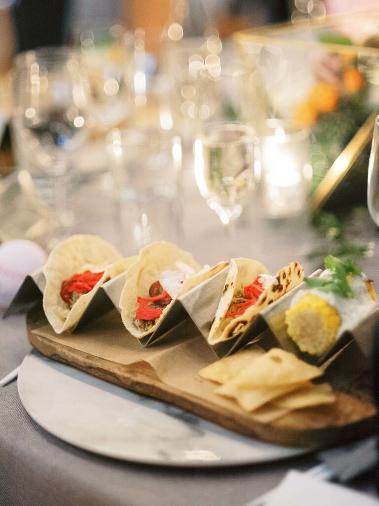 Reception table setting with a metal taco holder displaying a selection of delicious tacos and corn on the cob. 