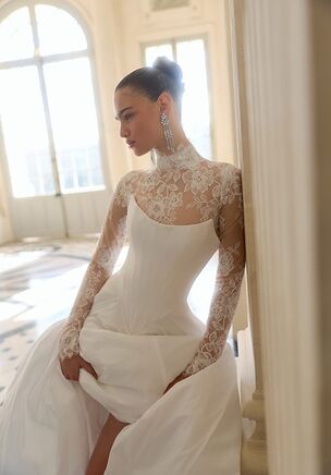 Luminous ivory taffeta and delicate lace combine to create a visual narrative in the Aster gown from WONÃ Concept. The base features a strapless bodice, straight neckline, dropped waist, and voluminous, floor-skimming skirt. An exposed open back details the structured silhouette. A removable, sheer high-neck bolero adds illusion detailing, a high collar, and long sleeves. Floral accents enrich the textile. It reads as a masterclass in modern bridal theater.