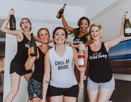 A bachelorette party wearing slogan shirts and holding bottles of champagne