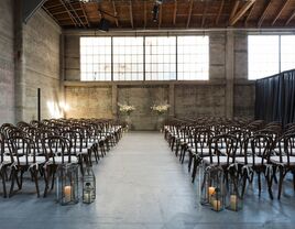 indoor wedding ceremony at minimalist industrial warehouse venue with large factory windows and concrete walls