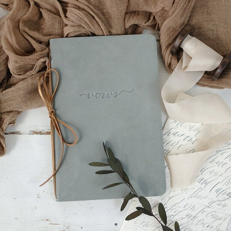 gray leather vow book embossed with vows in cursive script on the front and tied with brown leather binding