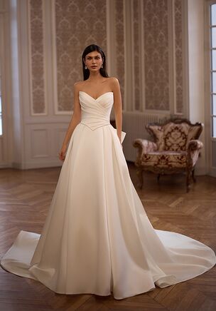 The Moonlight Collection J7008 wedding dress is a luxurious A-line gown in smooth satin, featuring a strapless ruched bodice with a pointed sweetheart neckline, basque waist, and delicate pearl trim. Finished with a voluminous box-pleated skirt and chapel train, this ivory or white design blends dramatic elegance with timeless, fairytale-inspired sophistication.
