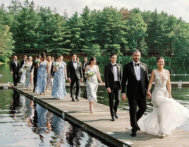 Bride and groom walking on dock with wedding party behind them