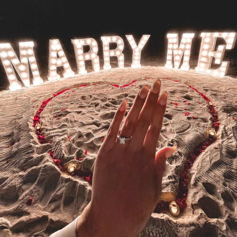 Engagement ring selfie in front of "Marry Me" letter lights
