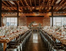 Inside view of rustic reception space with exposed red brick walls, twinkling lighting, wooden beams and a LED sign