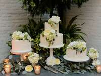 trio of white buttercream wedding cakes decorated with white flowers and greenery on a table