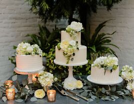 trio of white buttercream wedding cakes decorated with white flowers and greenery on a table