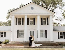 Happy newlyweds standing outside a grand white mansion at Prairie Meadows