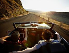 Young couple driving convertible at sunset