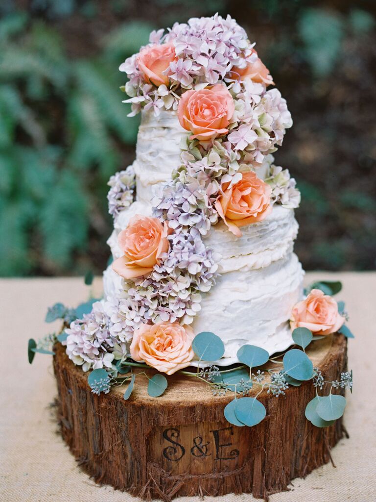 Three-tier rustic wedding cake with hydrangeas and roses on custom wood slice cake stand with initials