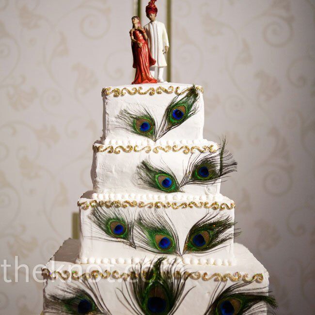 Each layer of the four- tiered buttercream cake was bordered with a gold scroll design and peacock feathers. The topper was fashioned  to resemble the couple.