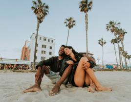 Couple smiling and sitting on beach together in Los Angeles