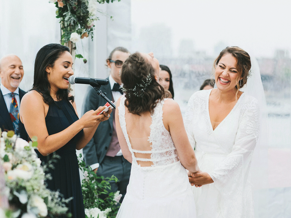 Brides mic'd up laughing with officiant during wedding vows.