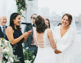 Brides mic'd up laughing with officiant during wedding vows.