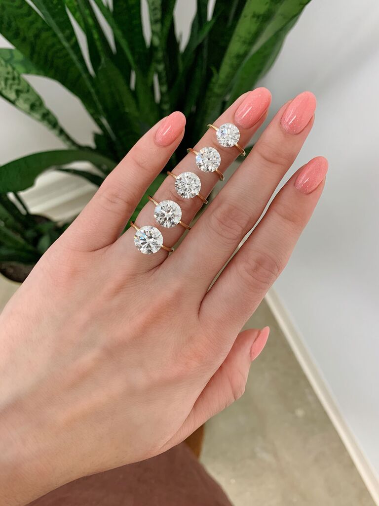 Five different diamond carat sizes in open ring settings on a finger