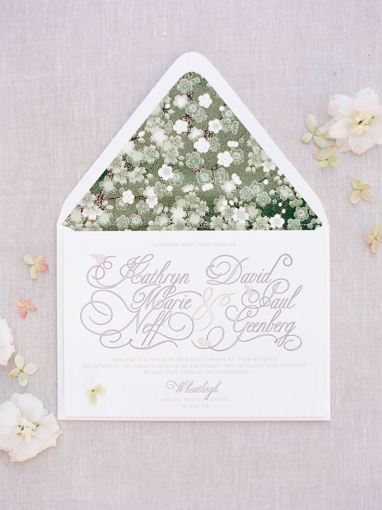 formal classic wedding invitation with embossed calligraphy against white background and green floral print envelope liner