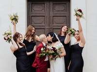 Bride with short hair and veil kissing spouse while surrounded by bridesmaids
