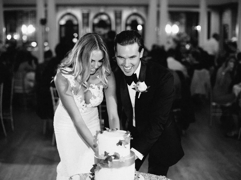 A black and white photo of a groom and bride cutting their wedding cake