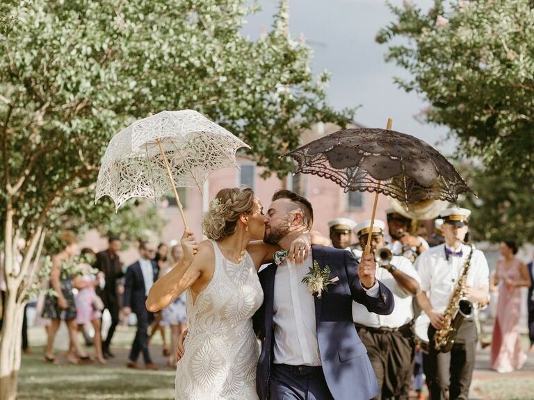 Newlyweds share a sweet kiss while holding fashionable lace parasols. 