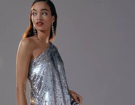 Model wears a long shimmery silver dress while looking over her shoulder. 