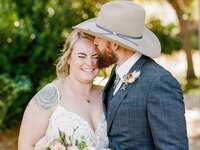 Man wearing a cowboy hat gives a sweet kiss on the cheek to his smiling bride. 