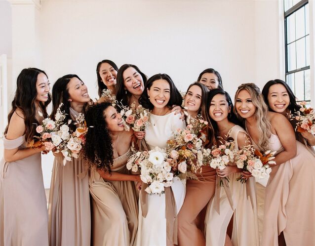 bride laughs with bridesmaids wearing neutral and blush bridesmaid dresses