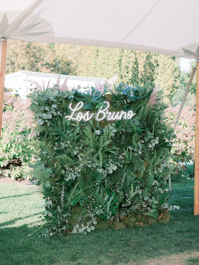 Greenery wall with last name neon sign at outdoor summer wedding