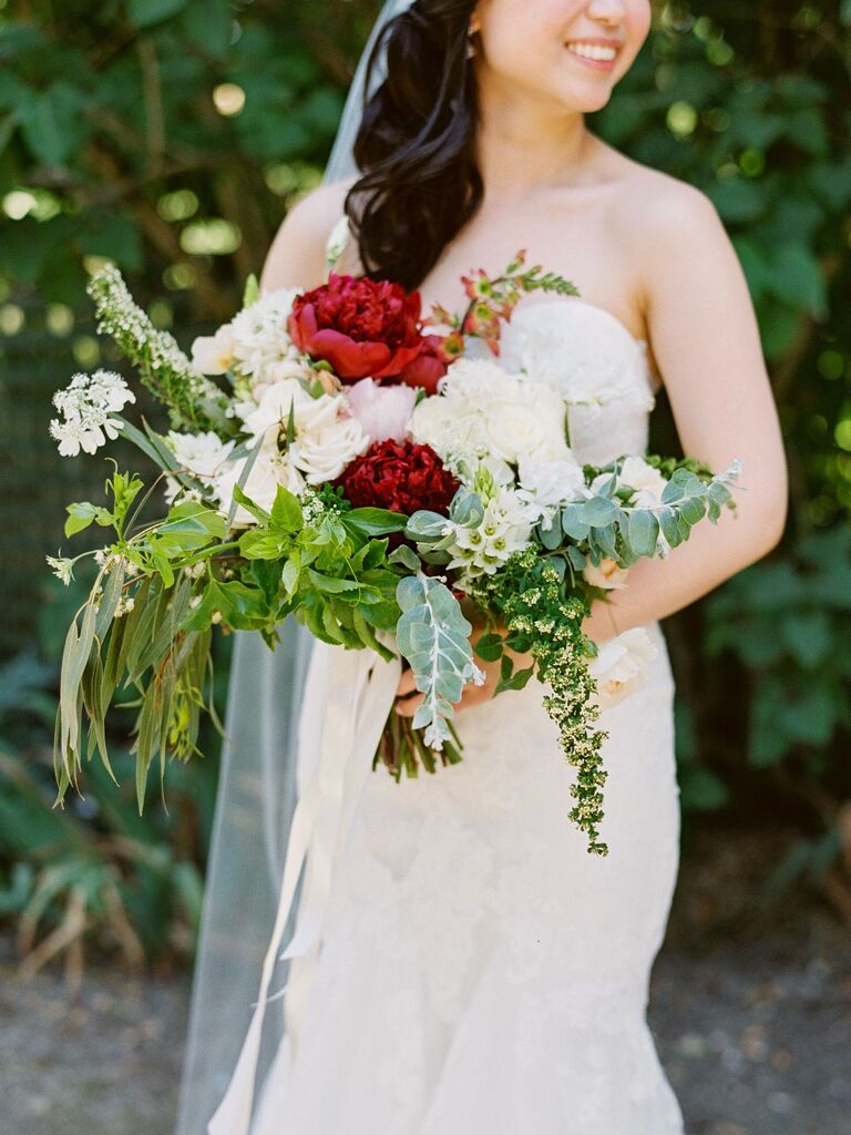 A bride holds an overflowing bouquet of white and red peonies.