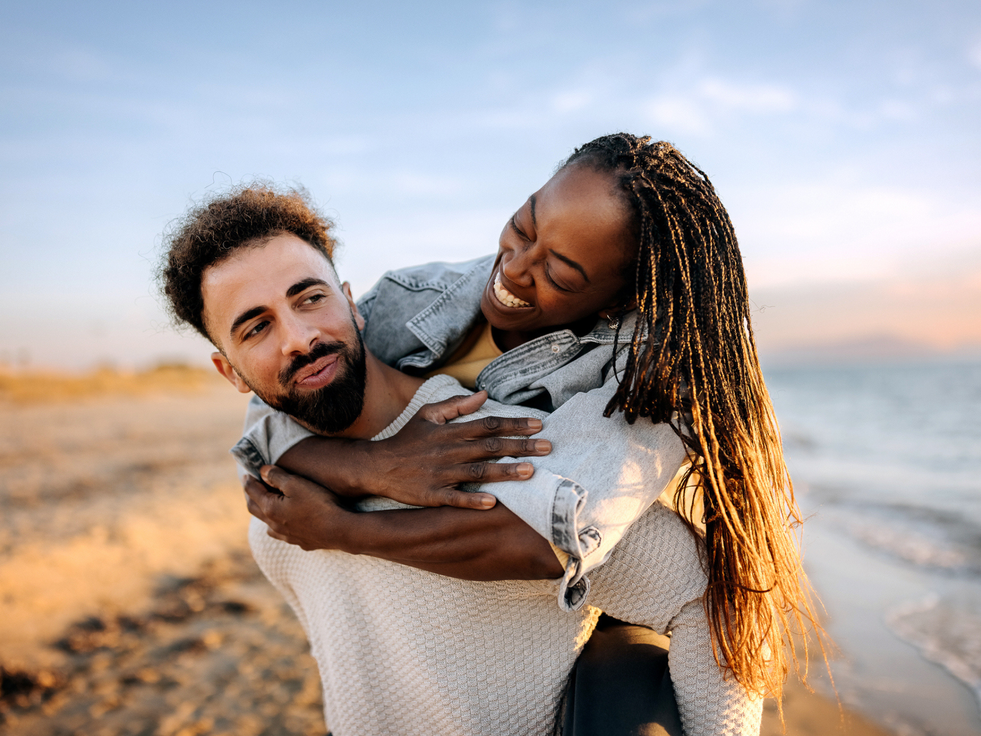 Man carrying partner on beach while smiling
