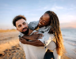 Man carrying partner on beach while smiling