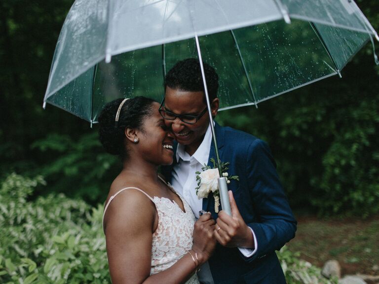 same sex couple two brides laughing and hugging under an umbrella at outdoor spring wedding