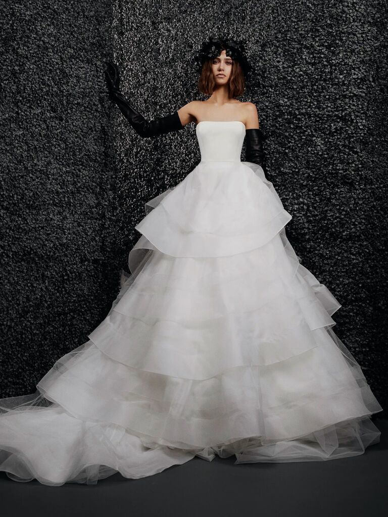 model stands against black backdrop wearing strapless ruffled tier ball gown with black leather gloves