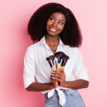 Woman holding makeup brushes in front of pink background