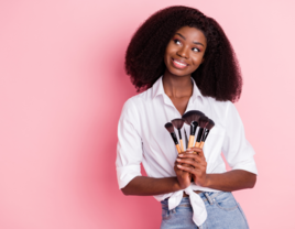 Woman holding makeup brushes in front of pink background