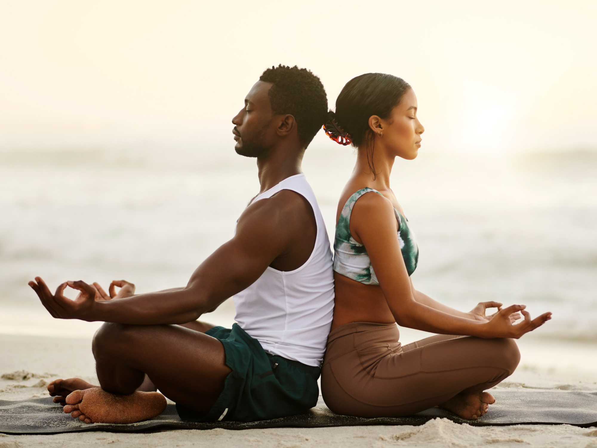 Couple sitting back to back meditating on the beach