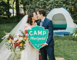 Couple holding a wooden sign that says, "CAMP Newlywed."