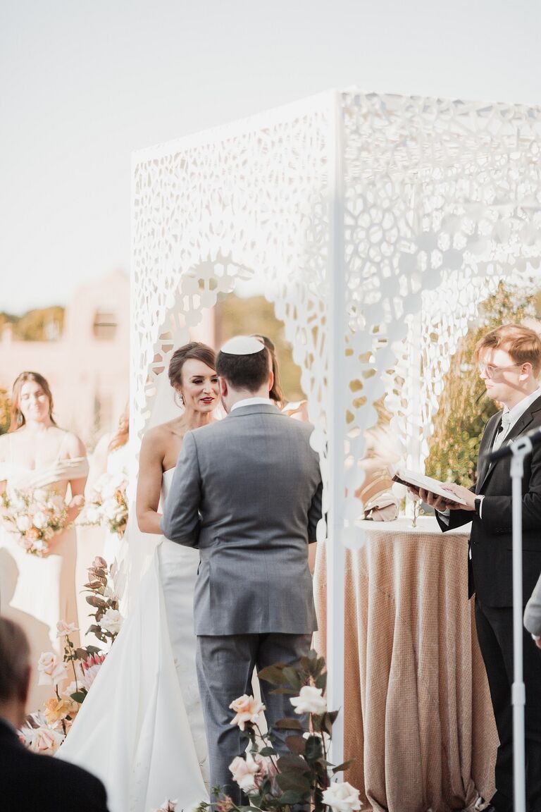 Couple holding hands in front of white chuppah with laser-cut pattern.