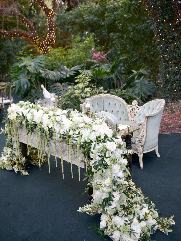 outdoor wedding sweetheart table idea with vintage loveseat and long garland with white flowers and greenery draped over the sides of the table